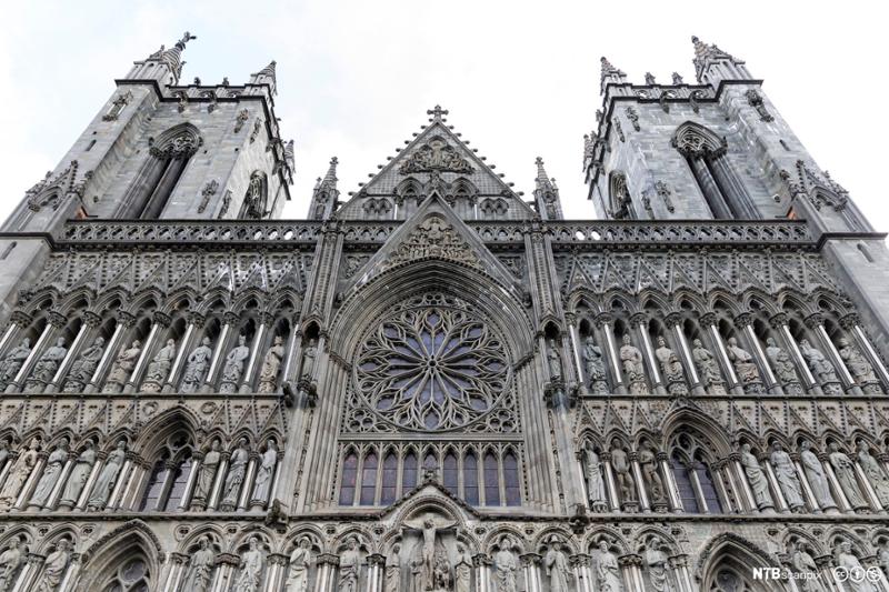 Fronten av en katedral i gotisk stil, med to tårn, helgenstatuer og et rundt glassmaleri i sentrum. Foto.