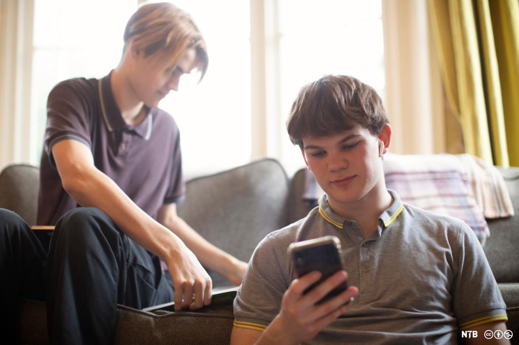 To tenåringar. Ein av dei ser på mobilskjermen sin. Foto.