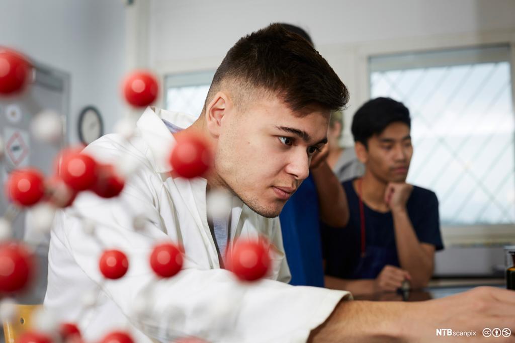 Mannlig elev jobber på kjemilab med molekylmodell i forgrunnen. Foto.