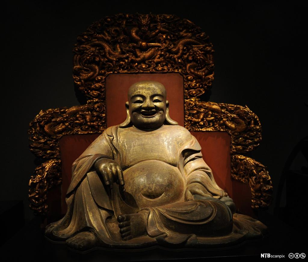 Statue av leende, tykk mann som sitter. Foto.