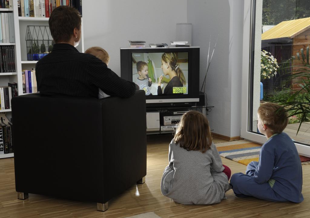 Far og barn sitter og ser på tv. Foto.