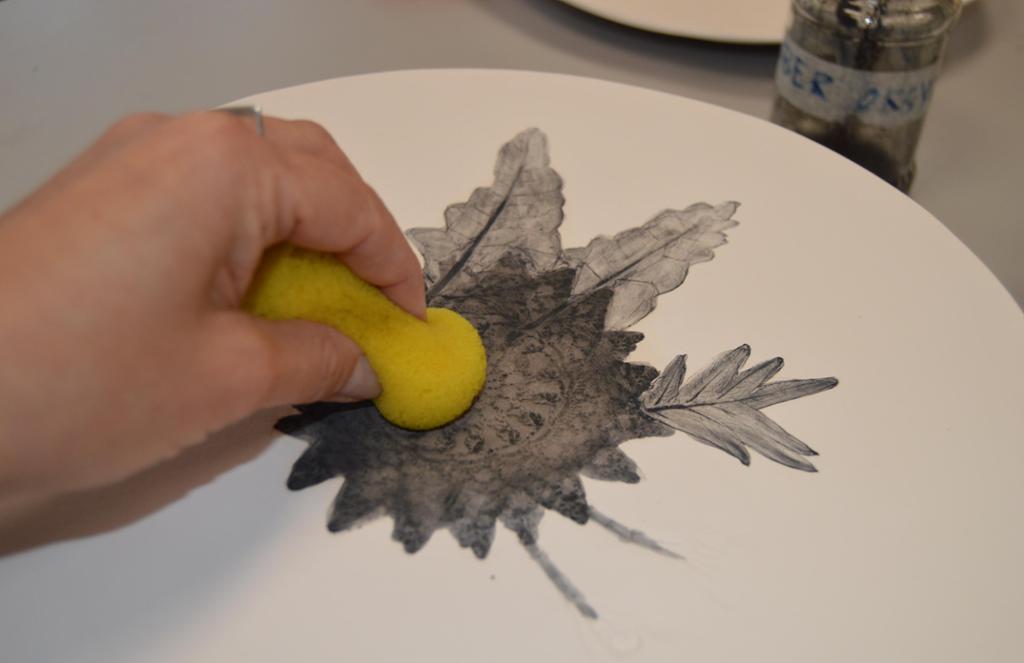 Overflødig mørk oksid vaskes bort med en gul svamp fra et lyst keramikkfat. Foto.