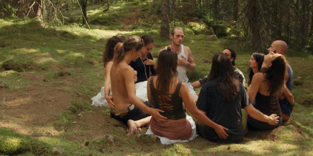 Ti unge voksne sitter i ring i en skog og holder rundt hverandre. Bildet er fra dokumentarfilmen "The Swedish Theory of Love". Foto.