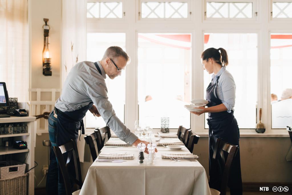 To servitørar dekkjer eit bord i ein restaurant. Foto.