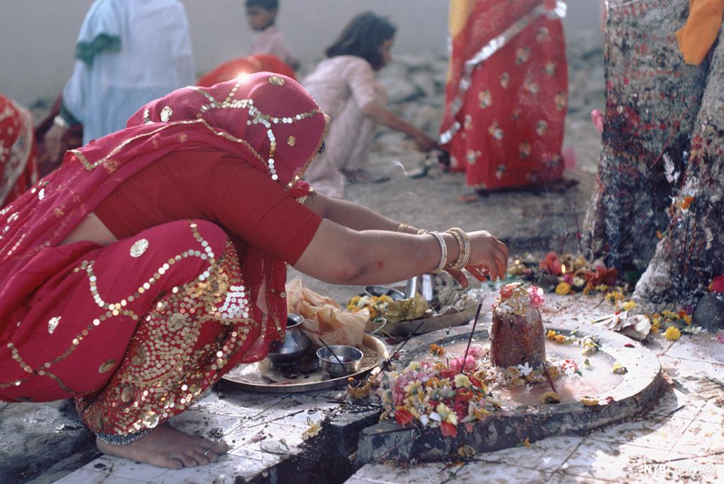 Kvinne i tradisjonell indisk klesdrakt legger blomster på en steinfigur. Foto.