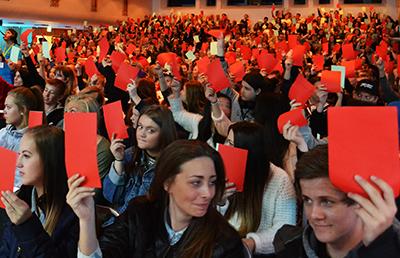 Ungdom som stemmer i Ungdommens PFU. En sal er full av ungdommer som holder opp røde eller grønne lapper. Foto.