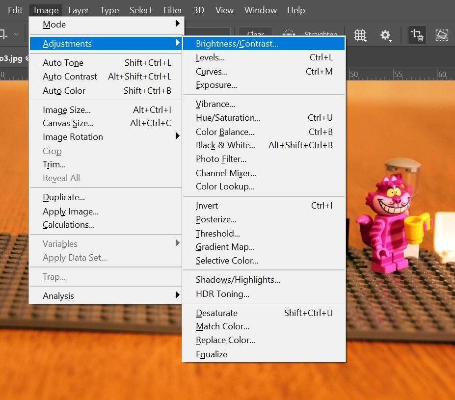 Utsnitt av biletredigeringsprogrammet Photoshop. På skjermen ser vi eit fotografi av Lego, mellom anna med Cheshire-katten. Over ser vi toppmenyen, der brukaren har valt Image og Adjustments. Undermenyen som dukkar opp, inneheld mange redigeringsverktøy. Hurtigtastane står til høgre. Skjermbilete.