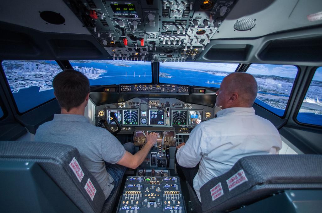 To personer sitter i cockpit i flysimulator. Foto.