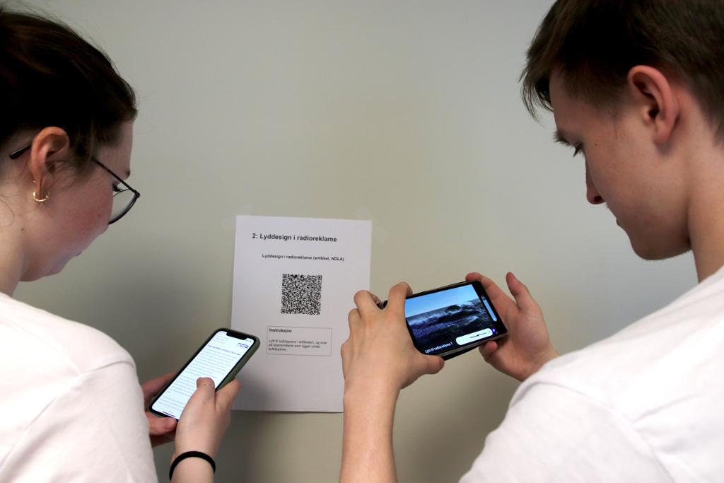 To elever står ved et ark med en QR-kode og skanner koden med hver sin mobil. Foto.