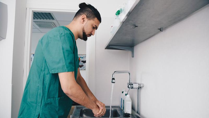 Mannlig sykepleier i grønt vasker hendene sine. Foto.