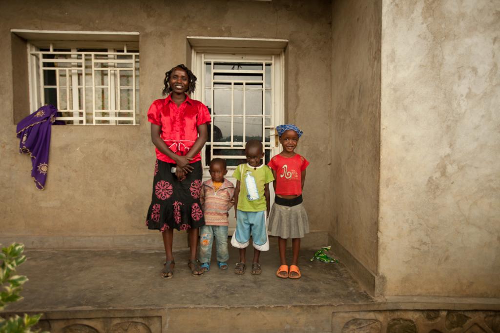Bilde av en familie på fire, en mor og tre barn, foran huset sitt i Rwanda. Foto.
