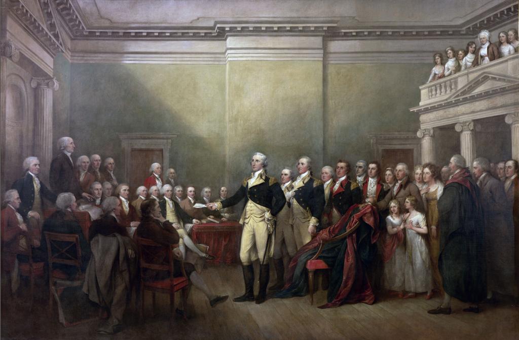 Painting: We see a large hall with columns and a balcony. The room is full of people in formal wear. There are two rows of seated men. All the men wear wigs. The man in the  centre of the picture is holding out a piece of paper. We understand from context that he is George Washington. 