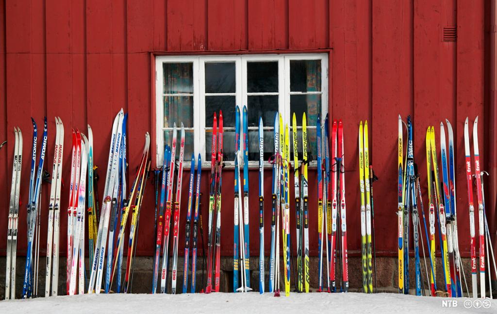 Mange par ski står plassert opp til en vegg. Foto.