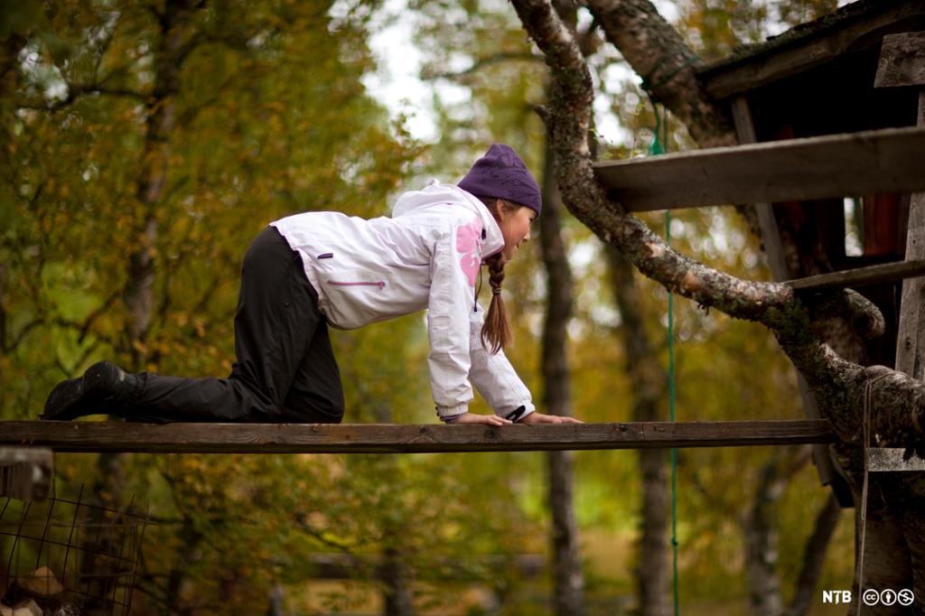 Ei jente balanserer på en smal planke ute i naturen. Foto. 
