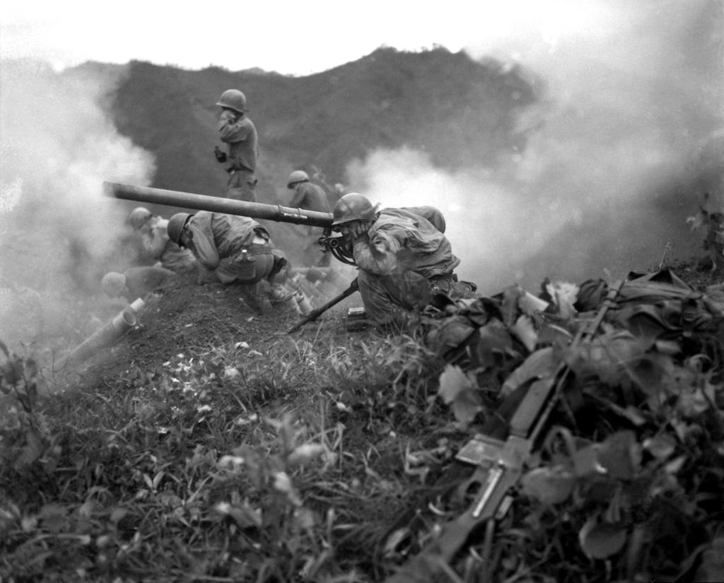 Hjelmkledde soldater med små kanoner ute i terrenget. Det er mye røyk fra ildgiving omkring dem. Svart-hvitt-foto.