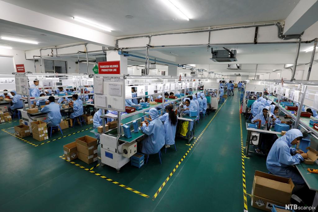 Arbeidere i beskyttelsesdrakter setter sammen mobiltelefoner i fabrikklokale. Foto.