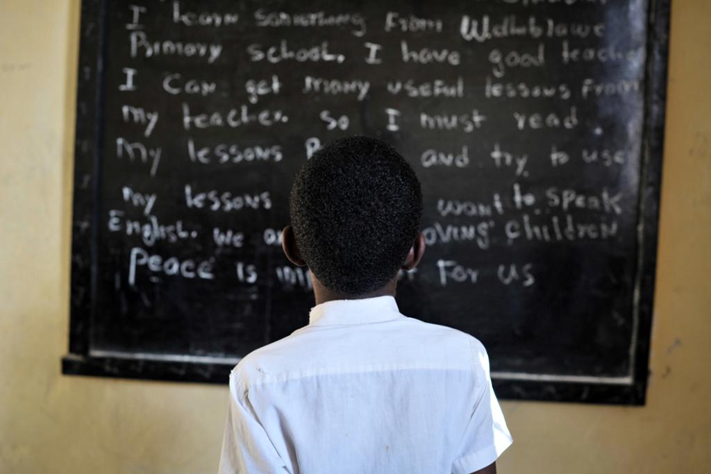 Ein gut står foran ei tavle på ein skule for interne flyktningar i Somalia. Foto. 
