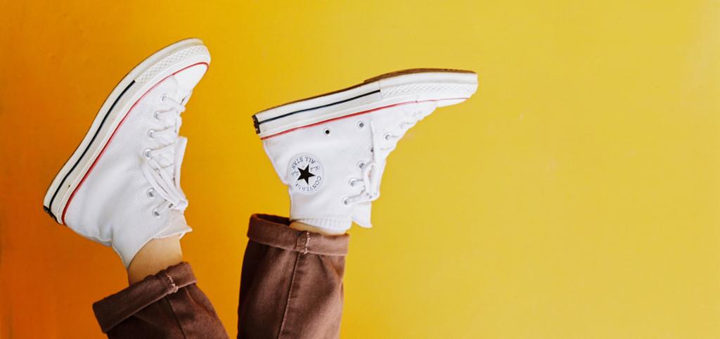 Utsnitt av beina til en person som har på seg hvite sko av typen Converse All Star. Bildet er dreid rundt så det ser ut som personen går opp ned. Foto.