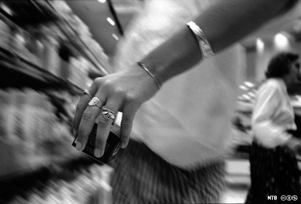 Svart-hvitt-bilde av en hånd som tar noe fra en butikkhylle. Foto.