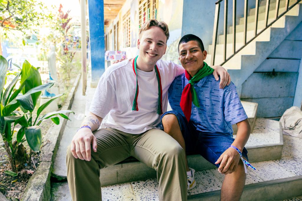 To unge menn sitter på ei trapp med armen over skuldra til hverandre. Den ene er fra Norge, og den andre er fra Colombia. Foto.