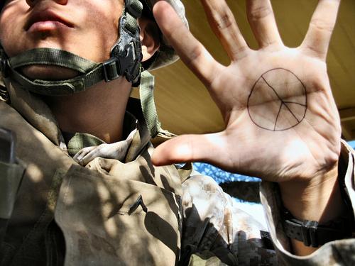 Foto av en soldat med uniform og hjelm som viser fram håndflata, der han har tegnet inn et fredssymbol.