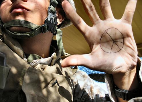 Foto av en soldat med uniform og hjelm som viser fram håndflata, der han har tegnet inn et fredssymbol.