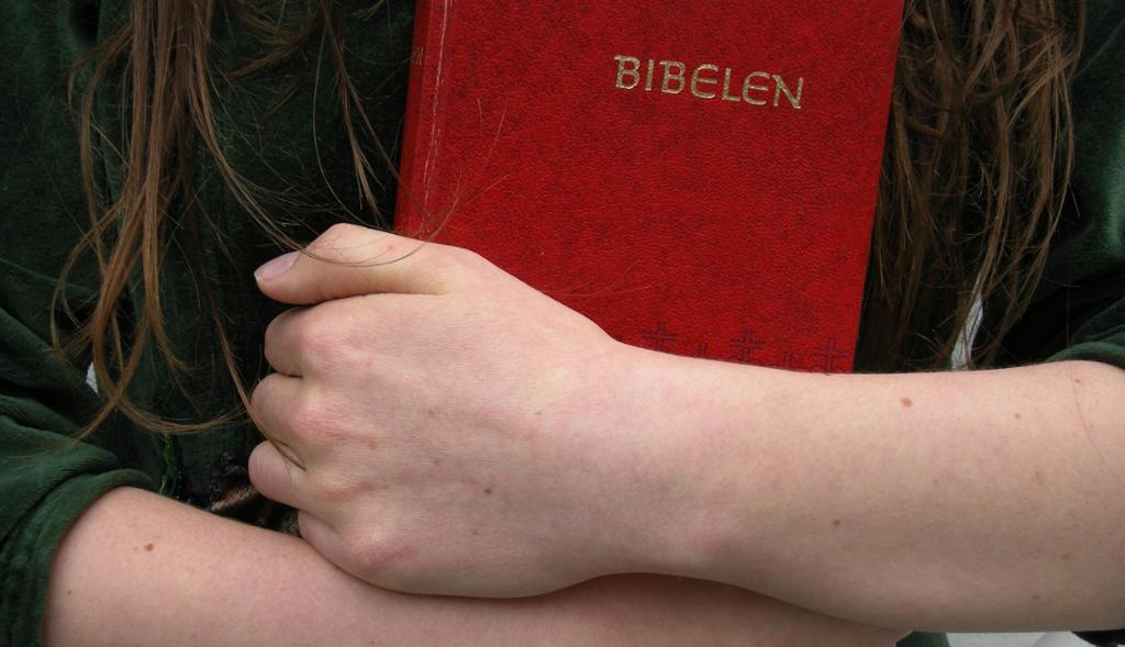 Ei jente trykkjer ein raud bibel til brystet. Foto.