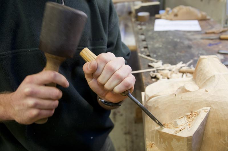 Treskjærer bruker klubbe og håndjern til å forme trearbeid. Foto.