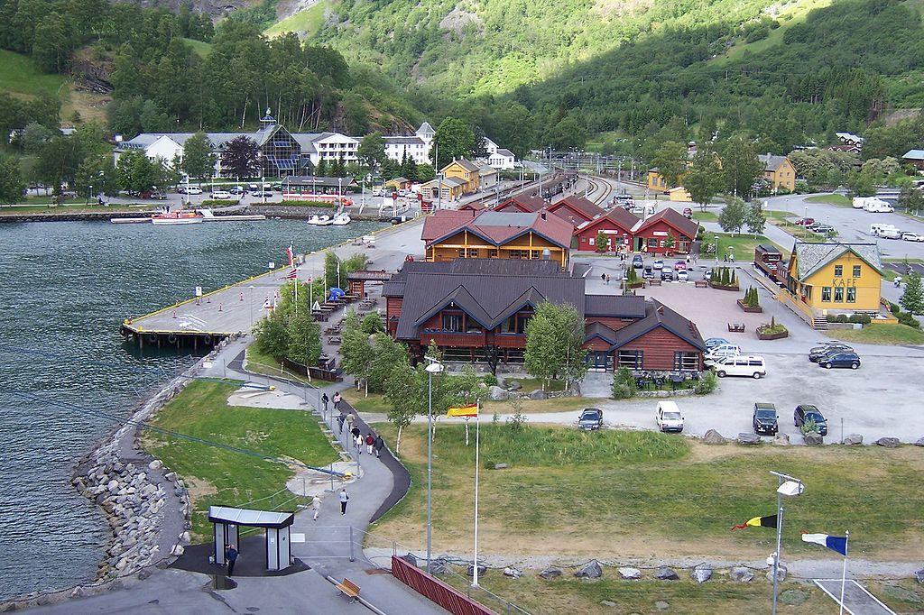 Flåm, en bygd innerst i Aurlandsfjorden. På bildet ser vi turistkaia med bebyggelse og parkeringsplasser, og Fretheim Hotel og Flåm jernbanestasjon i bakgrunnen. Foto.