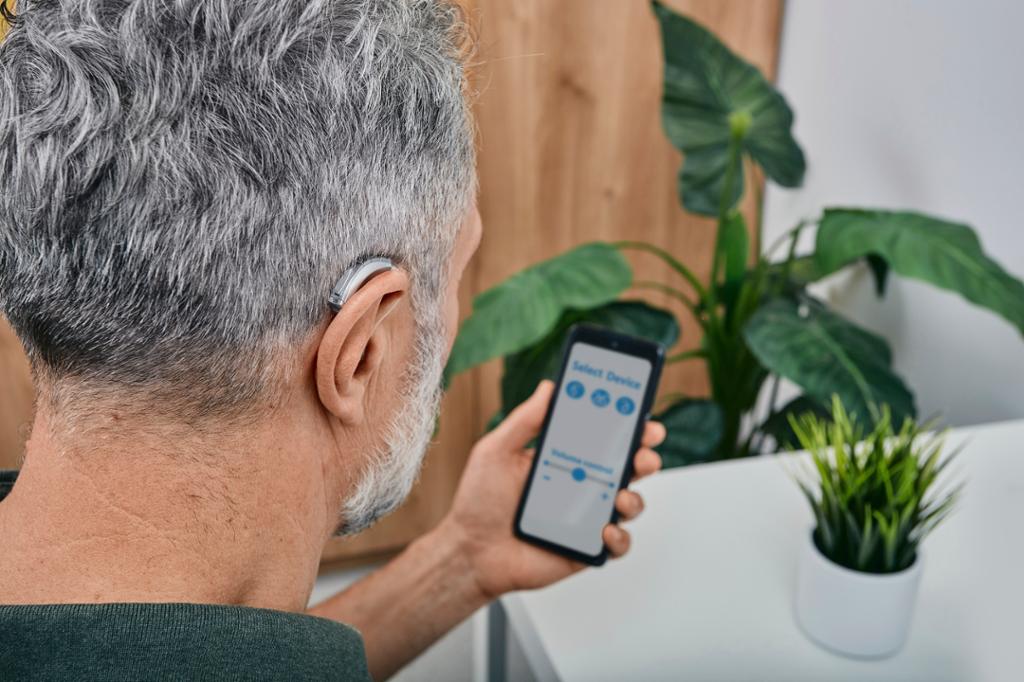 Person med høreapparat sjekker appen til apparatet på telefonen sin. Foto.