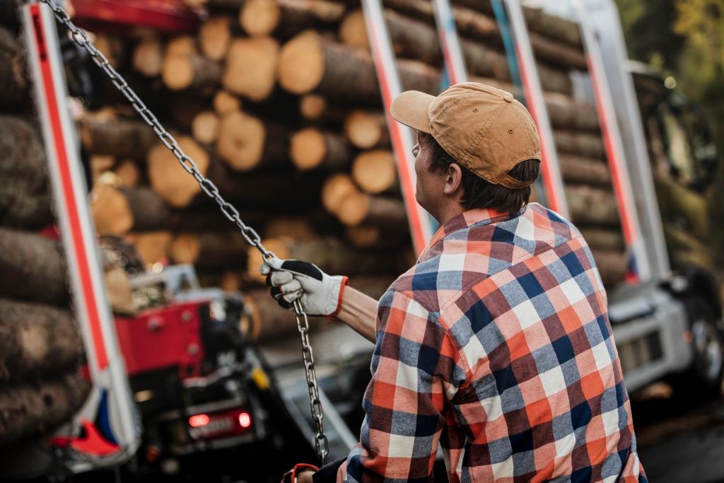 Bildet viser en tømmerbilsjåfør som sikrer tømmerlasten med kjetting.