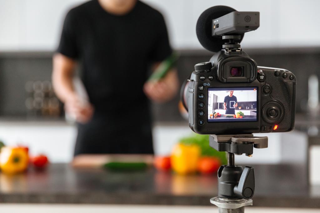 En ung mann med grønnsaker foran et kamera. Foto.
