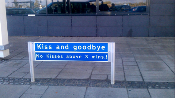 Bilete av eit skilt med påskrifta "Kiss and goodbye. No kisses above 3 mins.!" Foto. 
