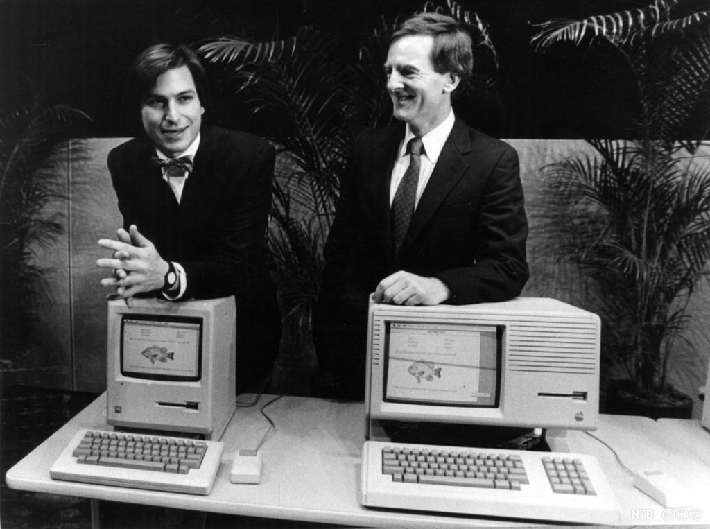 To dresskledde menn med hver sin gammeldagse datamaskin. Foto.