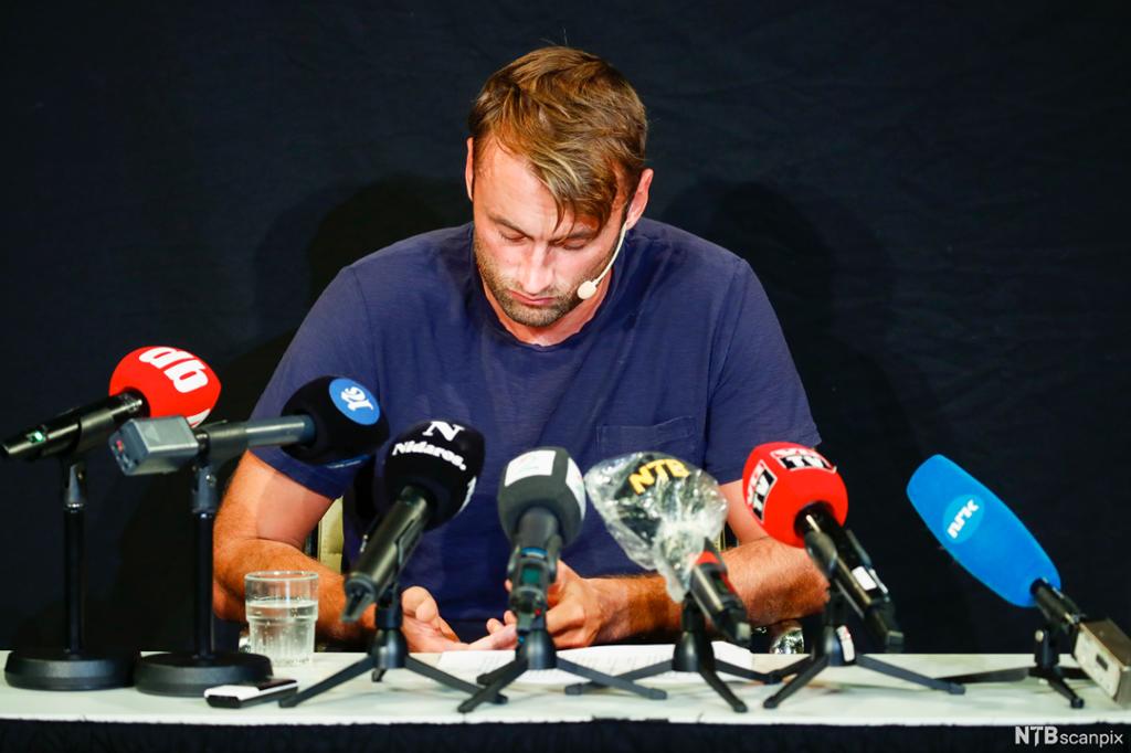 Petter Northug under pressekonferanse i Trondheim. Han sitter ved et bord med mange mikrofoner foran seg. Han ser nedtrykt ut. Foto. 