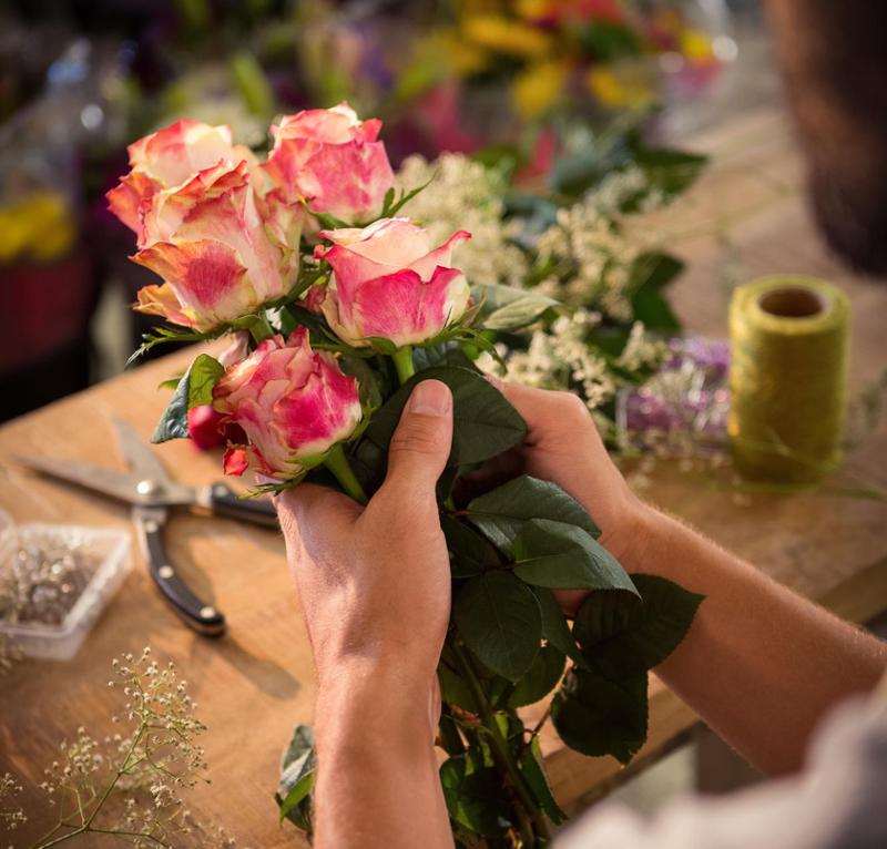 Hender som setter sammen en blomsterbukett. Foto.
