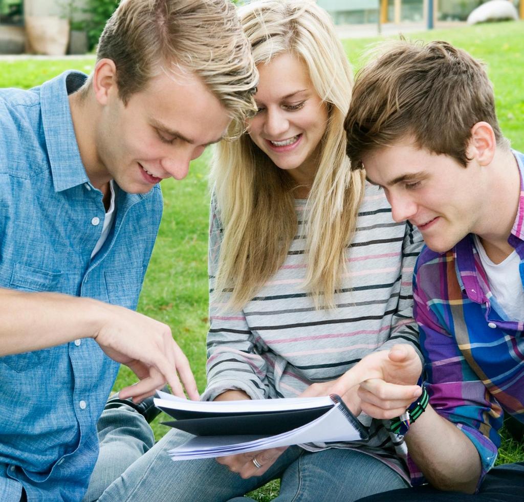 Tre elever snakker sammen rundt en notatbok. Foto.