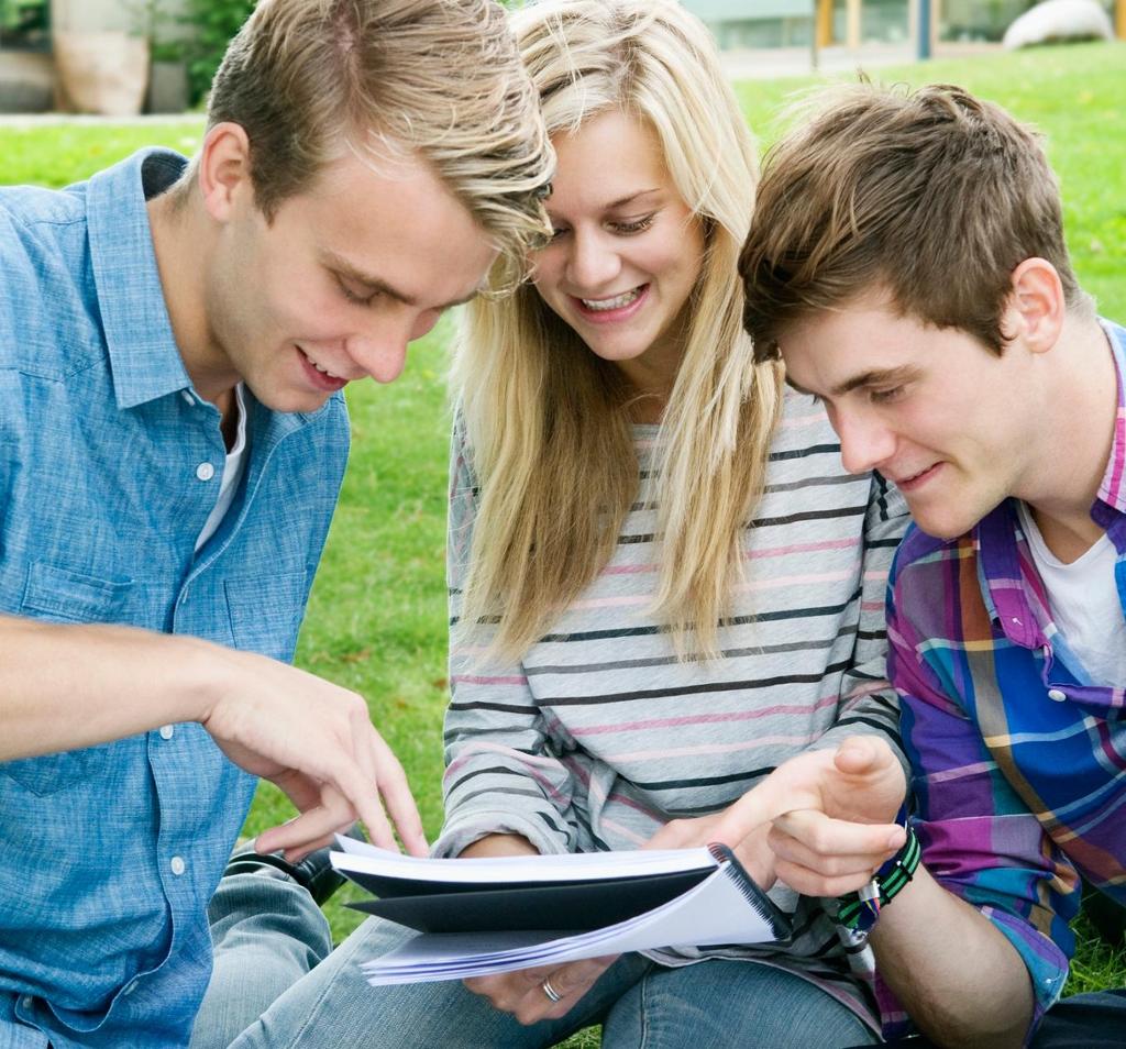 Tre elever snakkar saman rundt ein notatbok. Foto.