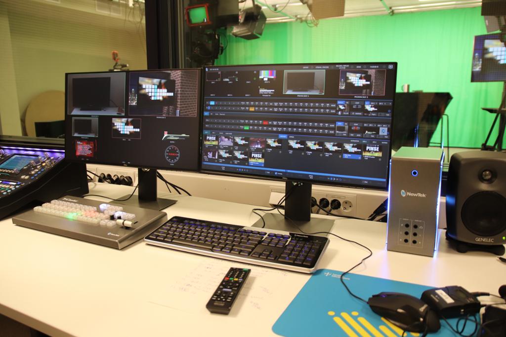 Pult i kontrollrom med flere skjermer, tastatur og bildemiks. I bakgrunnen er et tv-studio med grønnskjermvegg. Foto. 