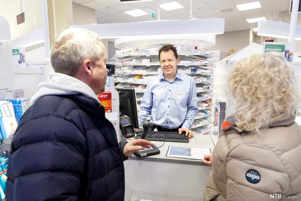 Mannlig farmasøyt bak disken hjelper kunder i et apotek. Foto.