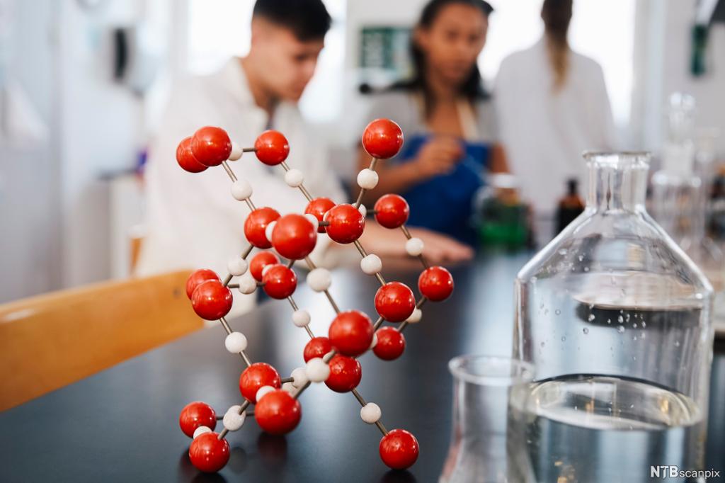 Molekylmodell står på lab-benk. I bakgrunnen ser vi elever. Foto.
