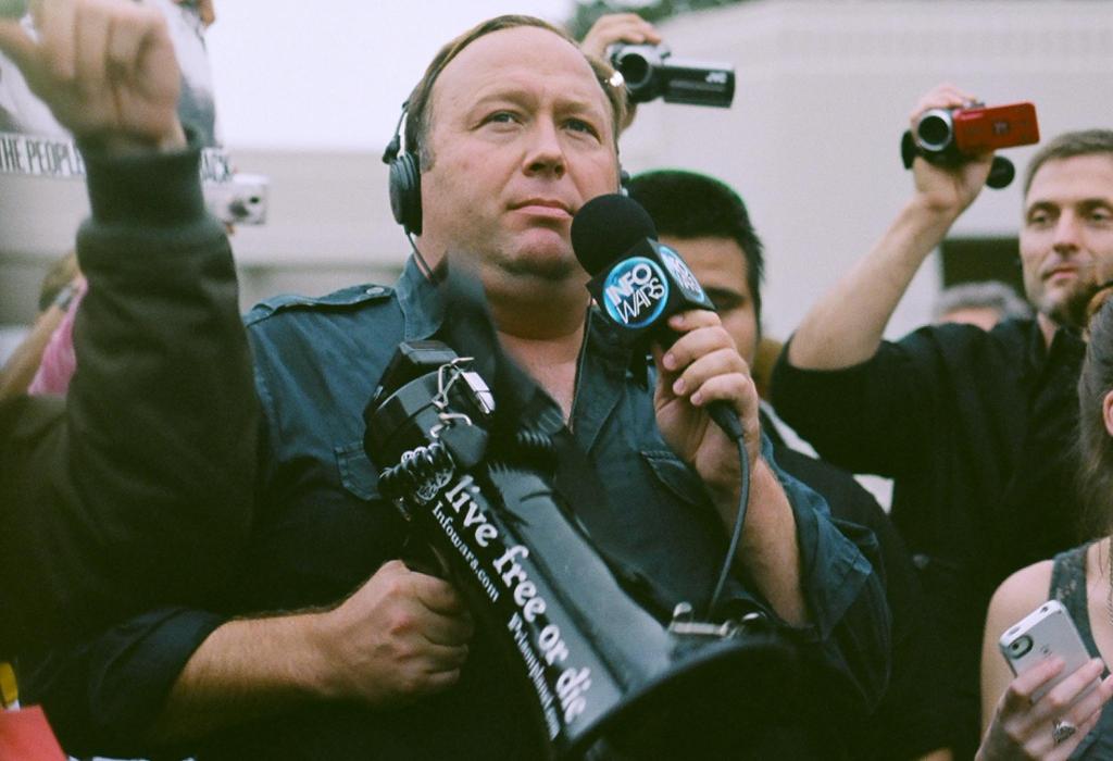 Mann med mikrofon og megafon. På megafonen står det "live free or die". Foto. 